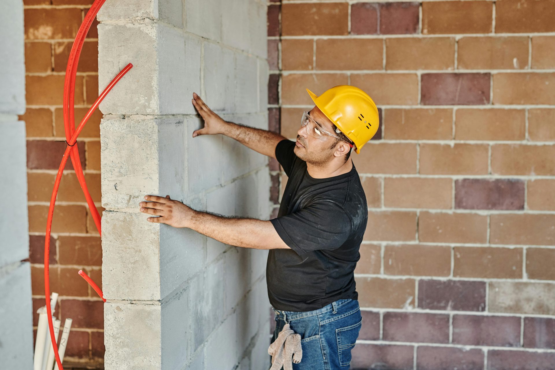 Un homme portant un casque vérifie un mur de briques sur un chantier de construction intérieur.